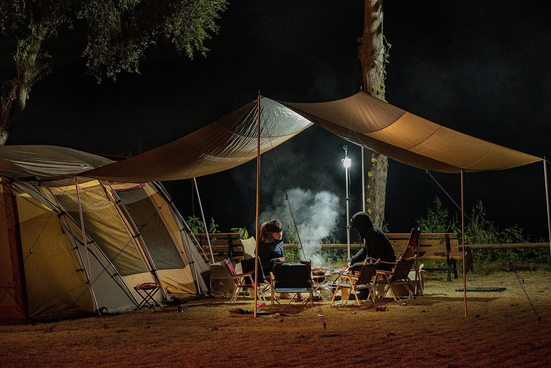 people sitting around a grill under a tent